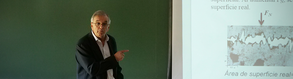 Profesor impartiendo clase con transparencias en aula con estudiantes de espaldas en la Facultad de Ciencias del Deporte