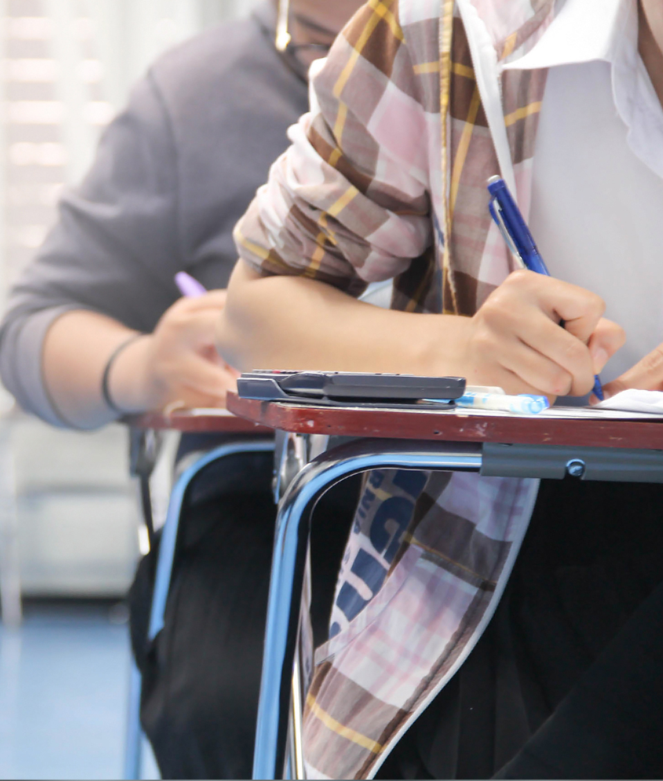 Estudiantes realizando un examen en un aula, en la mesa en primer plano se aprecia una calculadora científica